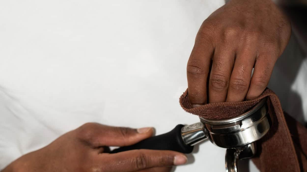 Een barista poetst de filterdrager van de espressomachine